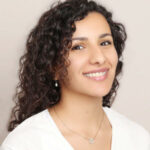 Headshot of a smiling woman with curly brown hair.